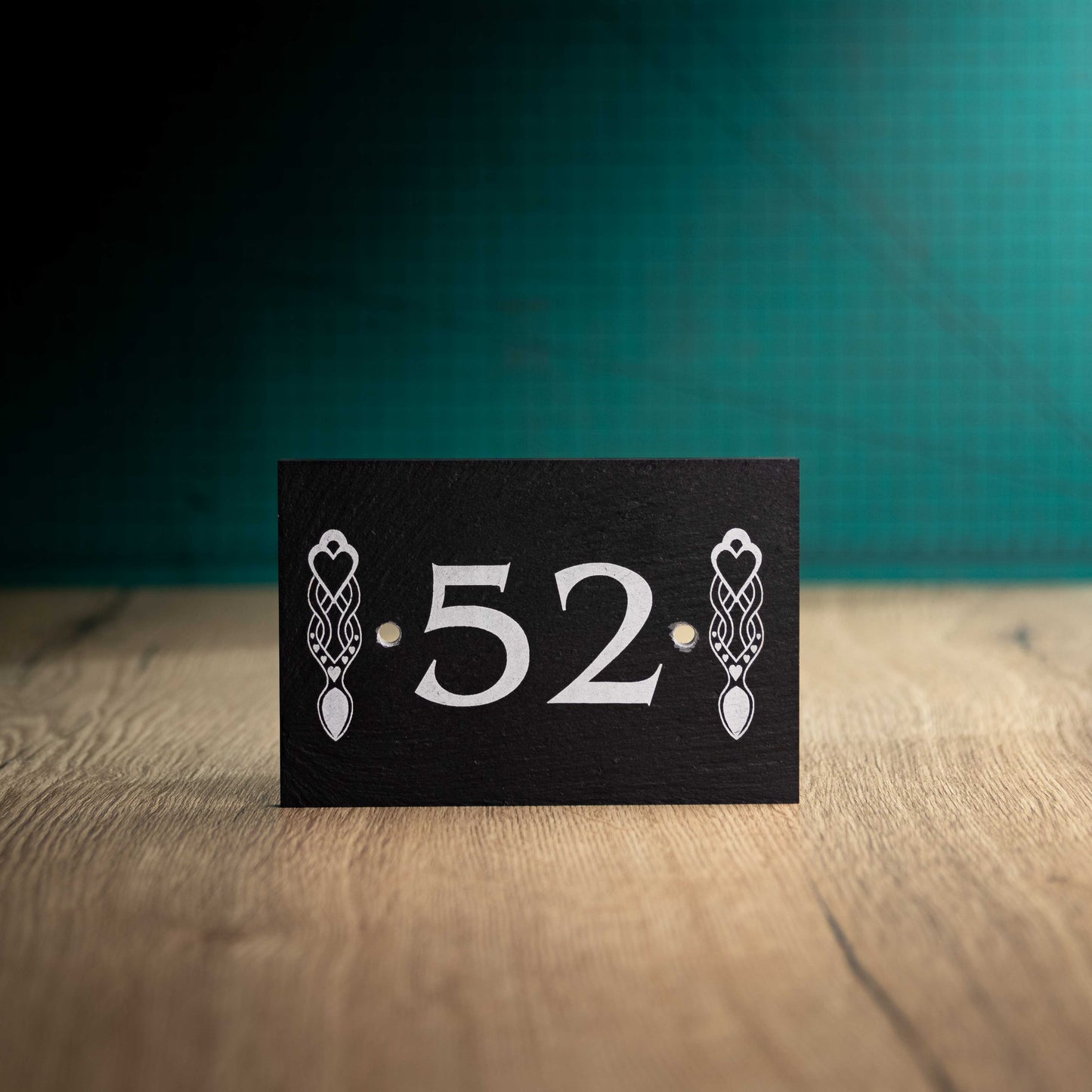 A laser-engraved slate house sign on a wooden surface and teal background. Rectangle 6" x 4"