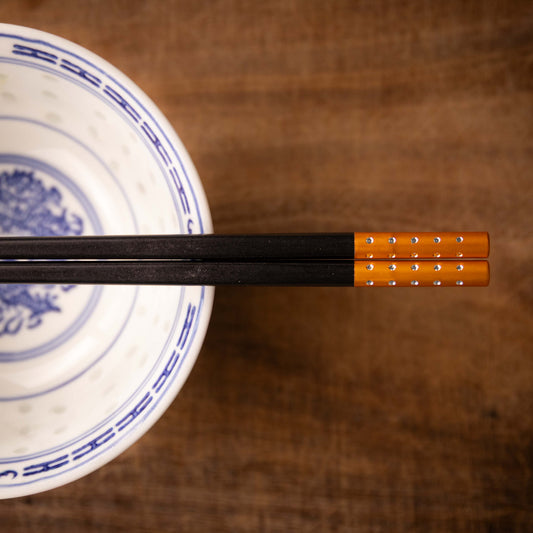 Black Wooden Chopsticks with a Orange coloured end on a Chinese rice bowl.