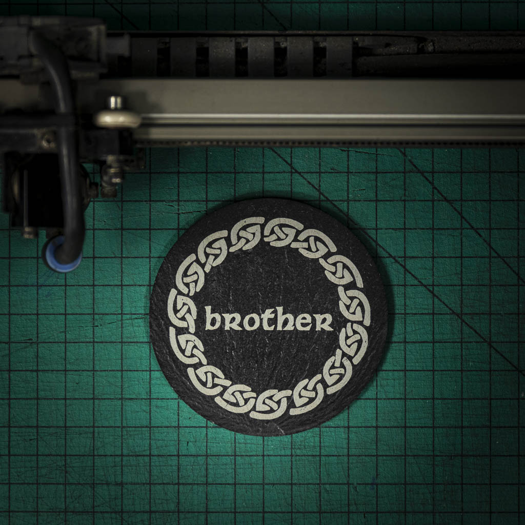 A Welsh slate coaster laser engraved with the word brother, inside a celtic knot