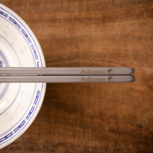 A pair of Personalised Brushed Titanium metal chopsticks placed on a Chinese rice bowl.