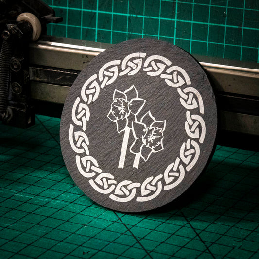 A laser engraved Welsh slate coaster with two welsh daffodil inside a celtic knot boarder