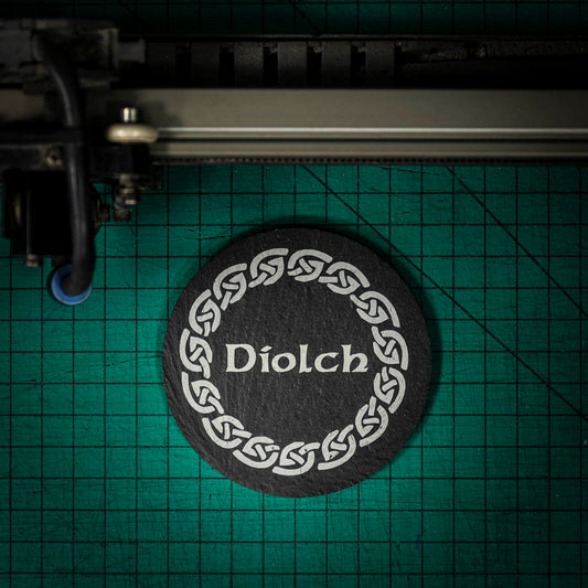 A Welsh slate coaster laser engraved with the welsh word for thank you, diolch, inside a celtic knot