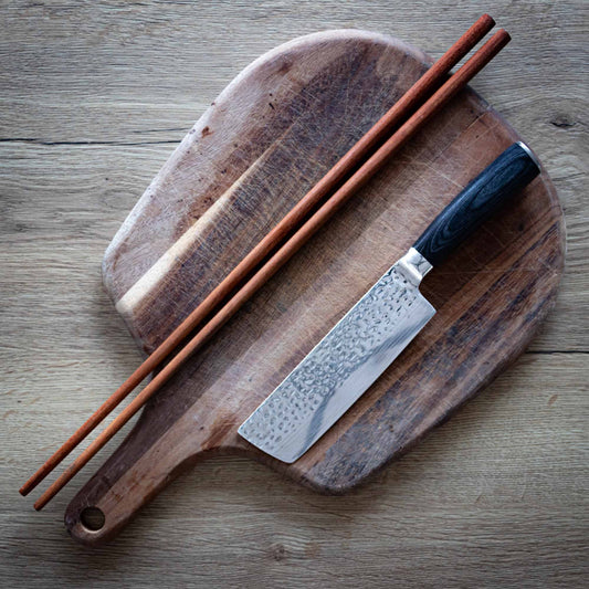 Long wooden cooking chopsticks on a chopping board next to a knife
