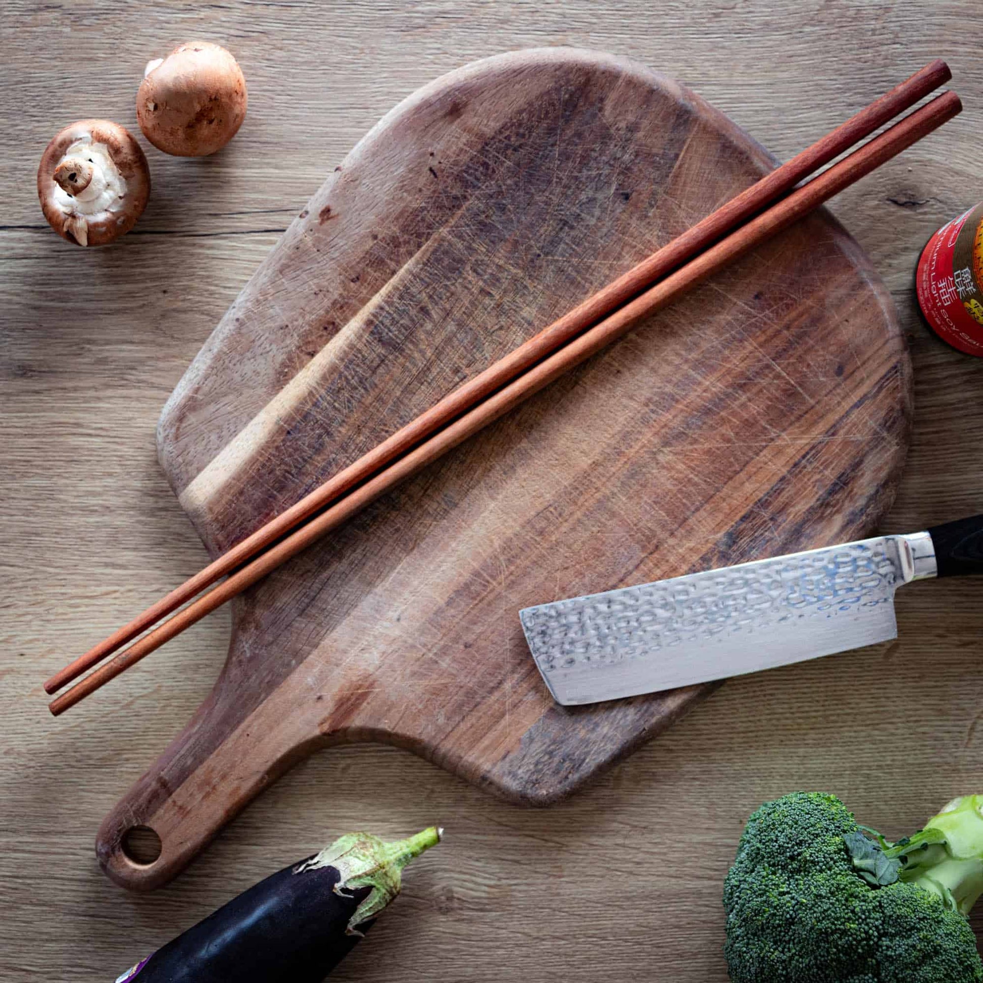 Long wooden cooking chopsticks on a chopping board surronded by food