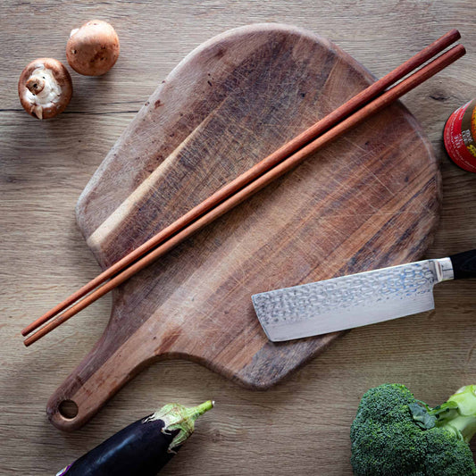 Long wooden cooking chopsticks on a chopping board surronded by food
