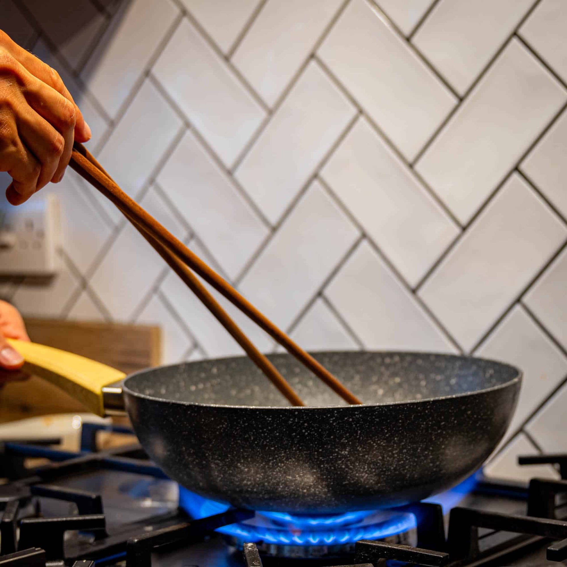 A person using long wooden cooking chopsticks to cook in a wok