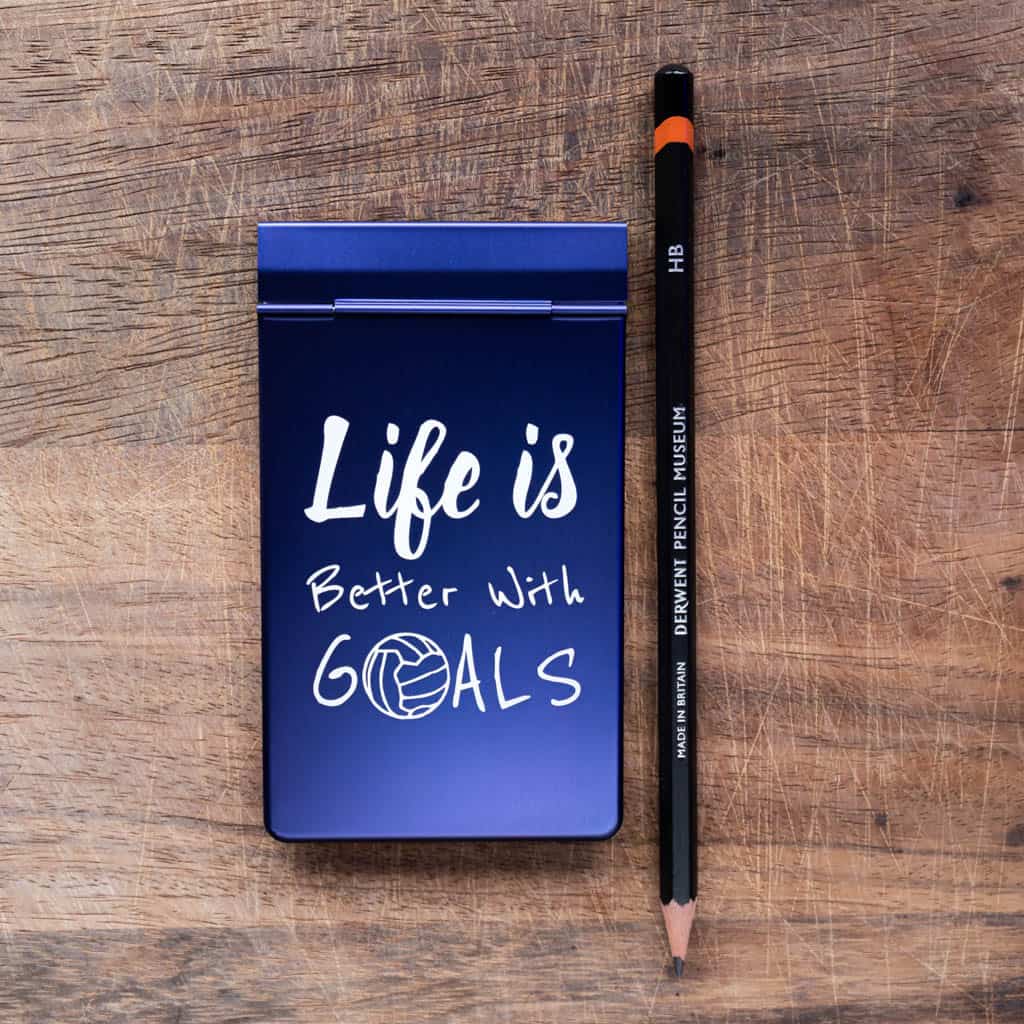 A notepad with a blue anodized metal cover with the phrase "Life is better with goals" laser marked onto the cover