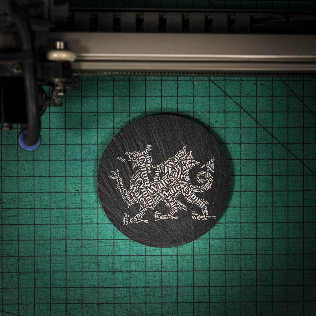 A laser engraved Welsh slate coaster with a dragon made up of the words Wales and Cymru