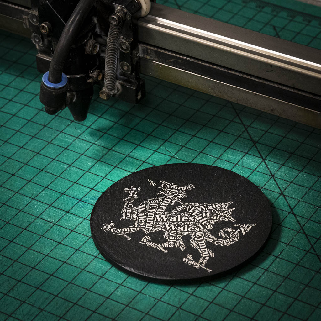 A laser engraved Welsh slate coaster with a dragon made up of the words Wales and Cymru