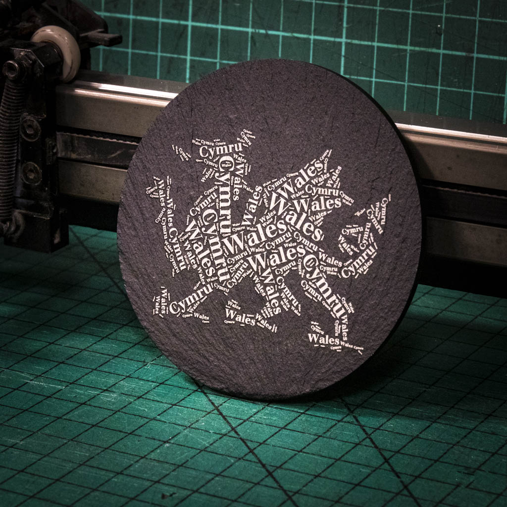 A laser engraved Welsh slate coaster with a dragon made up of the words Wales and Cymru