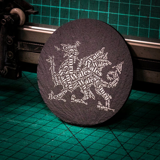 A laser engraved Welsh slate coaster with a dragon made up of the words Wales and Cymru