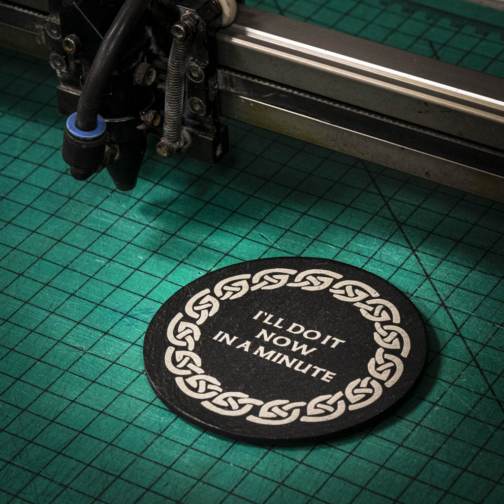 A laser engraved Welsh slate coaster with the words I'll do it now in a minute inside a celtic knot boarder