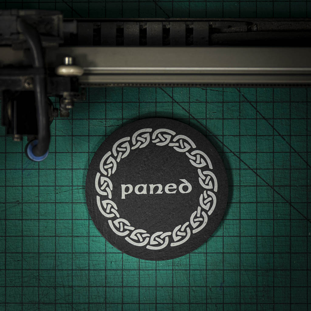 A Welsh slate coaster laser engraved with the welsh word for a cuppa, paned, inside a celtic knot