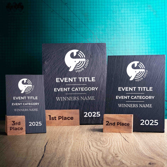 Three laser-engraved, eco-friendly, wooden and slate trophies called Solet. The Solet Award has a base made of two wooden pieces on either side of a square piece of Welsh Slate. The trophy is personalised with Event information and a logo.