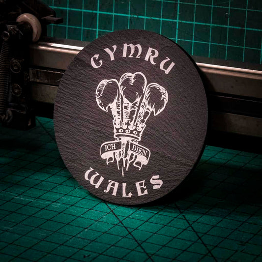 A laser engraved Welsh slate coaster with the welsh three feathers in the center and the words cymru and wales