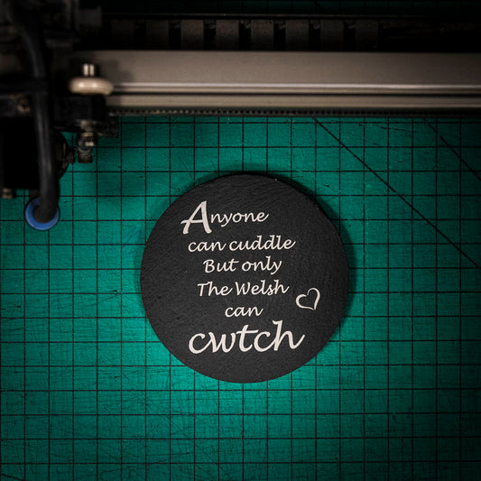 A laser engraved Welsh slate coaster with the words anyone can cuddle but only the welsh can cwtch