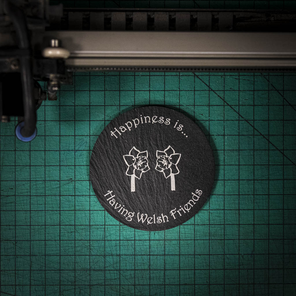 A laser engraved Welsh slate coaster with two welsh daffodils and the words happiness is having welsh friends