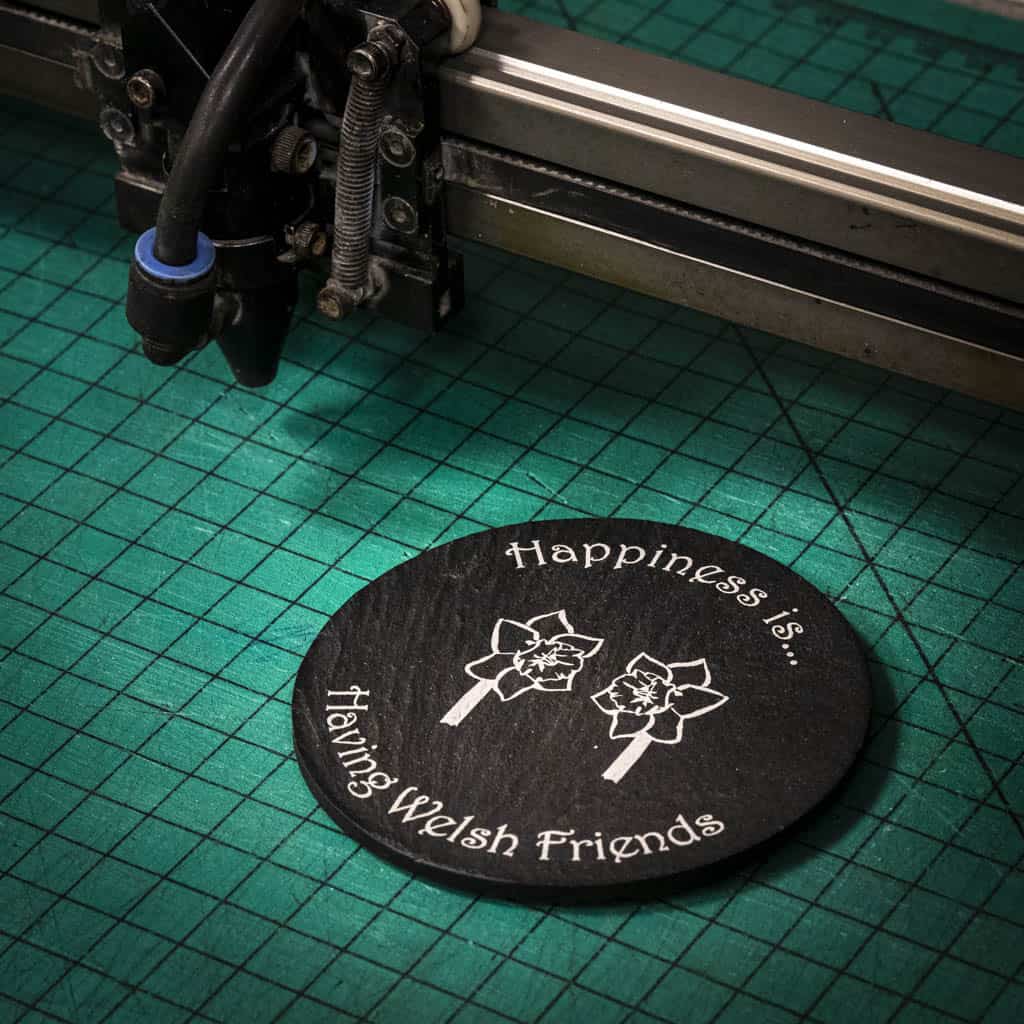 A laser engraved Welsh slate coaster with two welsh daffodils and the words happiness is having welsh friends