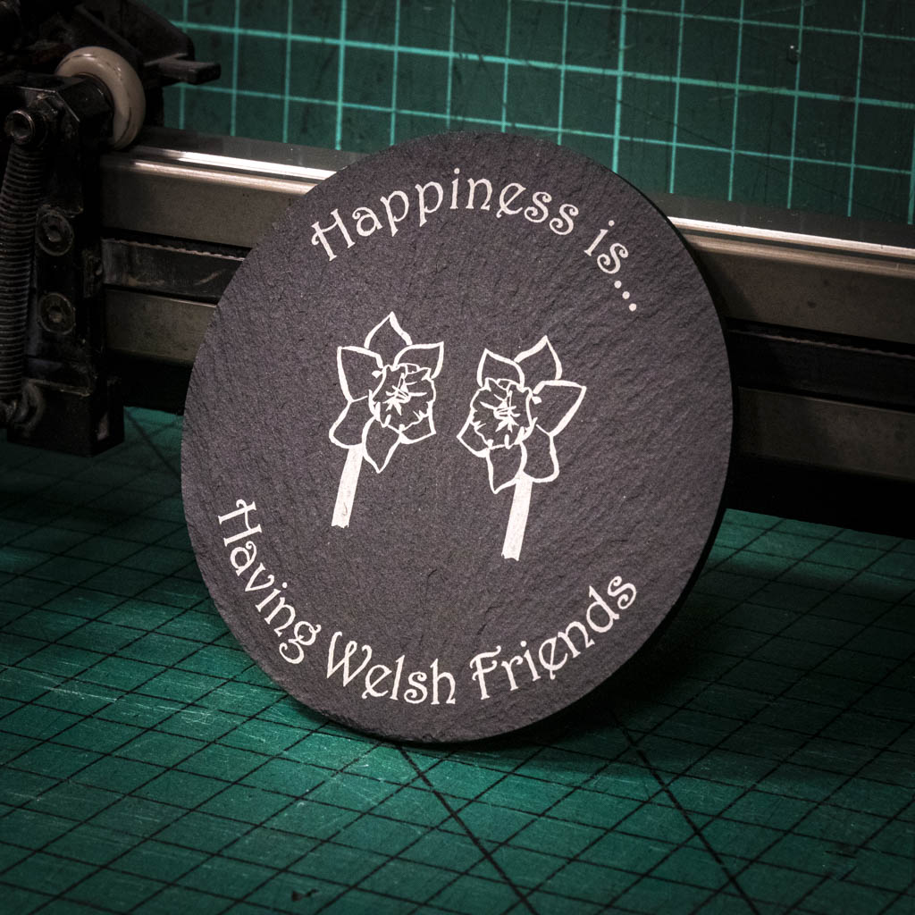 A laser engraved Welsh slate coaster with two welsh daffodils and the words happiness is having welsh friends