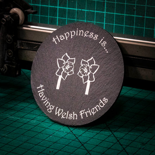 A laser engraved Welsh slate coaster with two welsh daffodils and the words happiness is having welsh friends