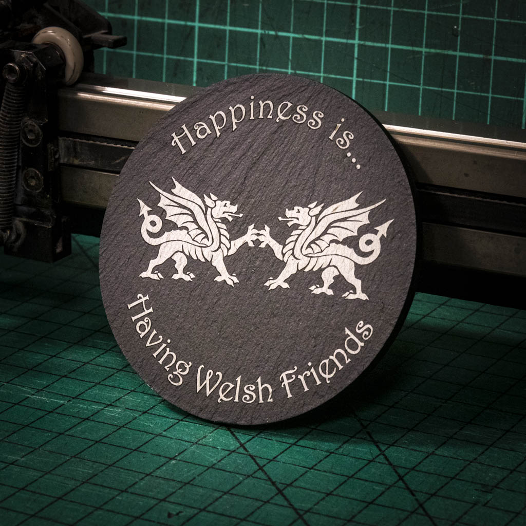 A laser engraved Welsh slate coaster with two welsh dragons and the words happiness is having welsh friends