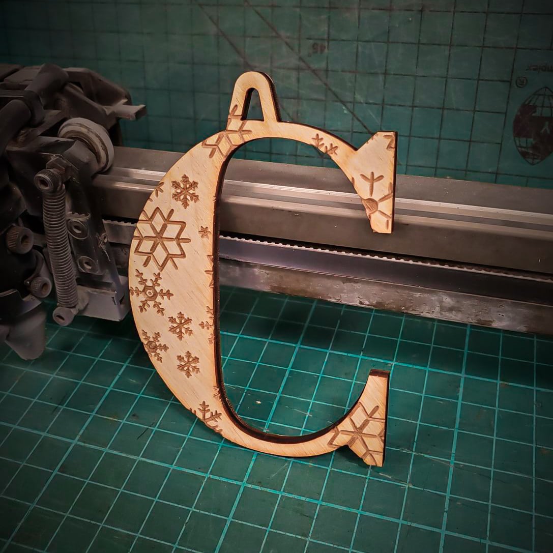A wooden Christmas tree decoration laser cut into the shape of the letter "C" and engraved with snowflakes