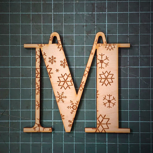 A wooden Christmas tree decoration laser cut into the shape of the letter "M" and engraved with snowflakes