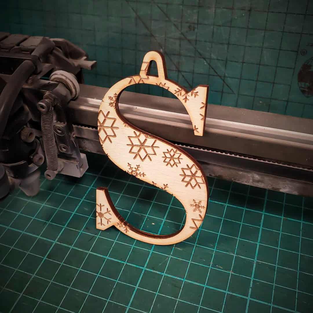 A wooden Christmas tree decoration laser cut into the shape of the letter "S" and engraved with snowflakes