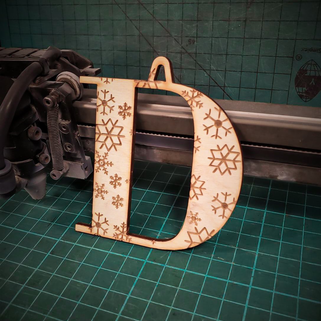A wooden Christmas tree decoration laser cut into the shape of the letter "D" and engraved with snowflakes