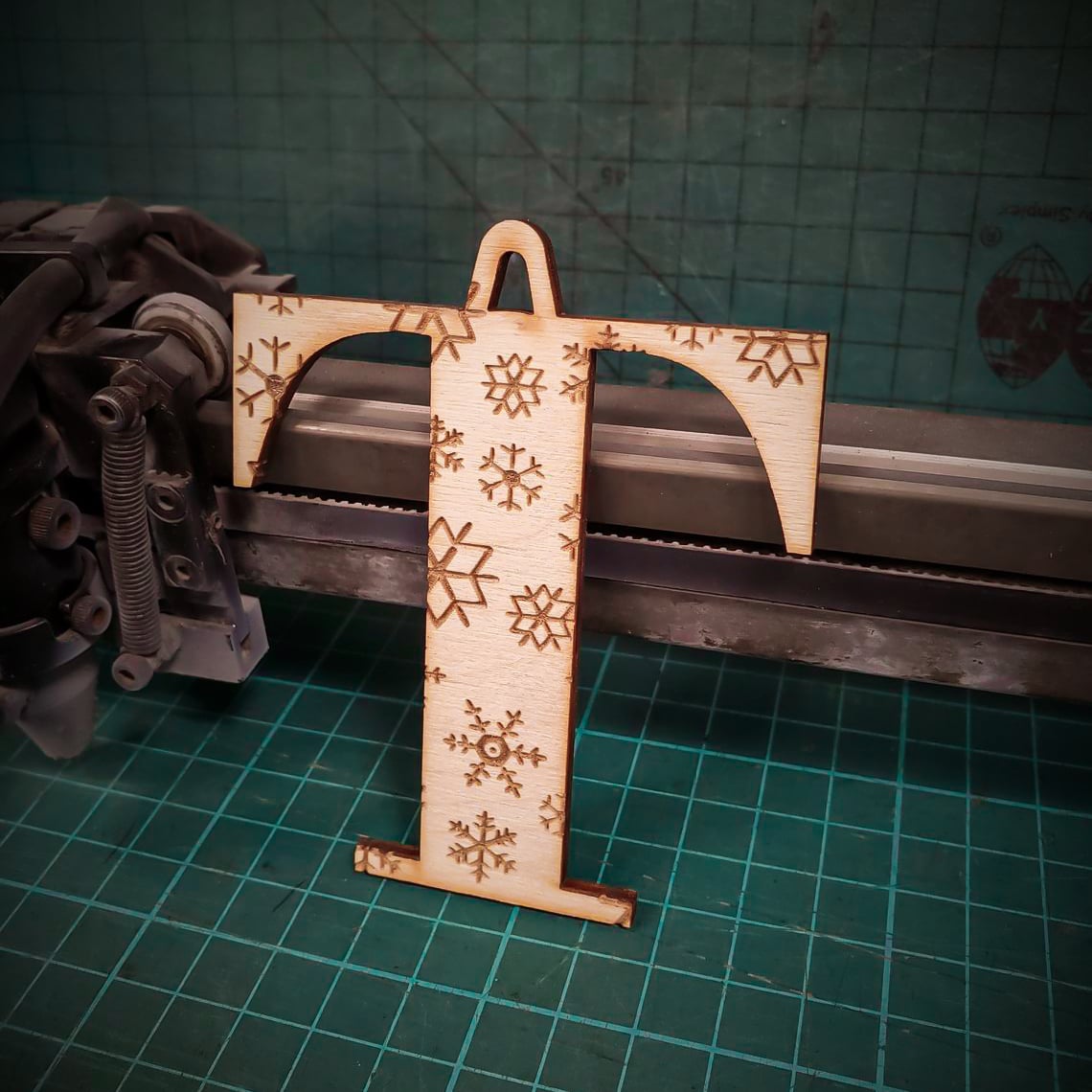 A wooden Christmas tree decoration laser cut into the shape of the letter "T" and engraved with snowflakes