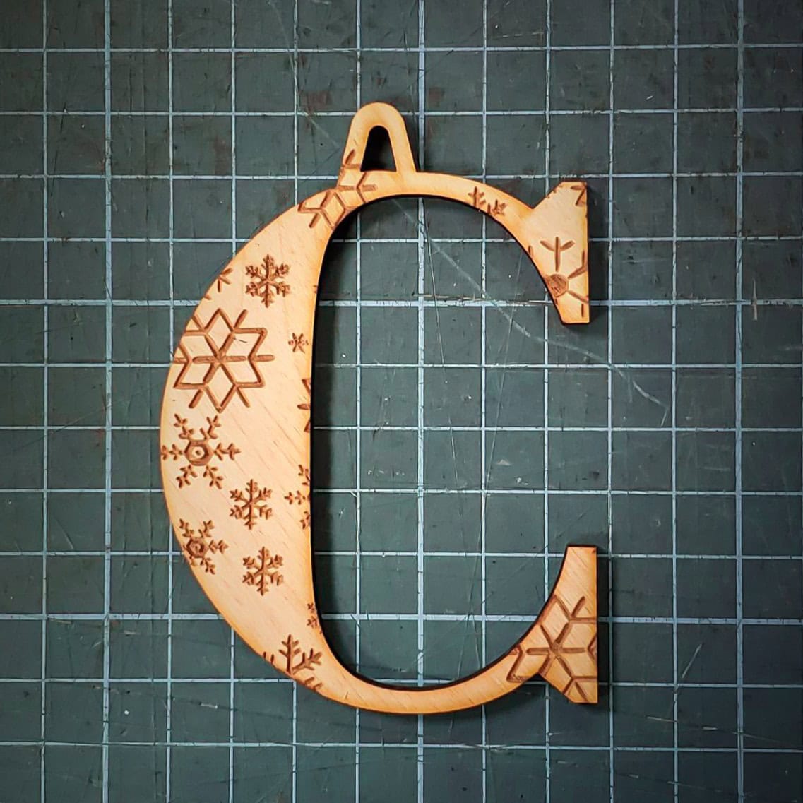 A wooden Christmas tree decoration laser cut into the shape of the letter "C" and engraved with snowflakes