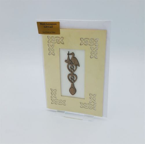 A laser cut card with an affixed wooden lovespoon with a stork