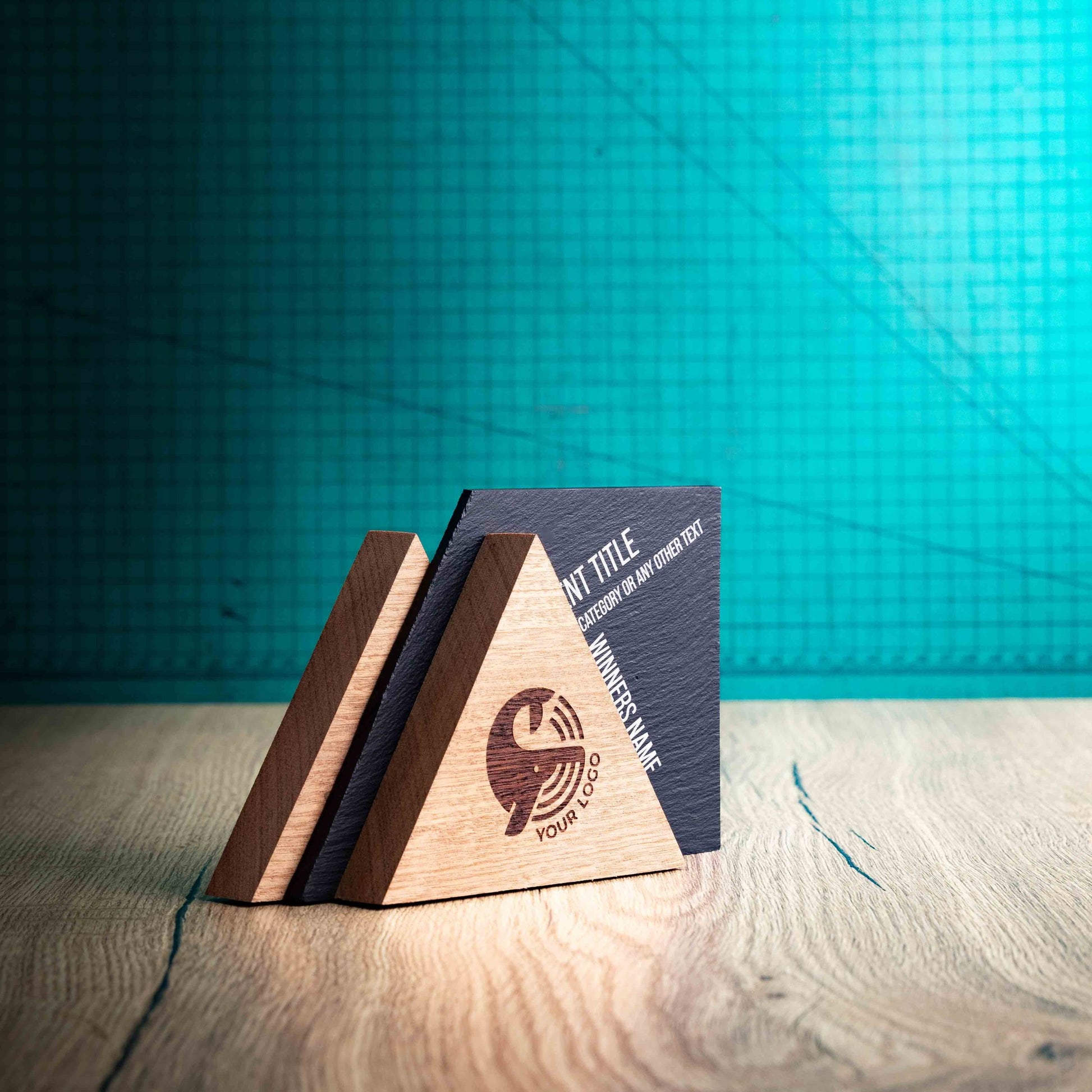 A side angle of the Alpine Award, a laser-engraved, eco-friendly, wooden and slate trophy. The Alpine trophy has two triangular wooden pieces on either side of a square piece of Welsh Slate. The trophy is personalised with Event information and a logo. 