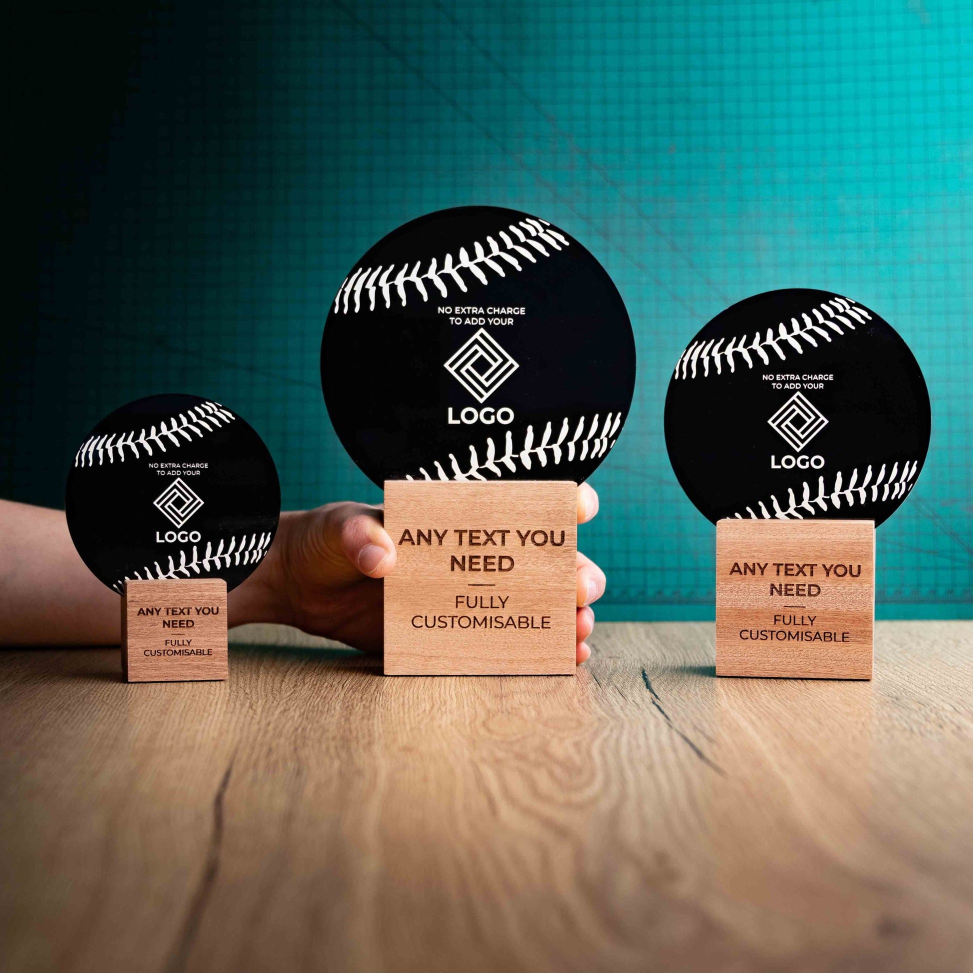 Three Baseball trophies with custom text and logos, on eco-friendly wooden bases, with a black Perspex Baseball mounted on top, featuring fully customisable areas for text and logos with a hand holding the large trophy to give a perspective of the size.