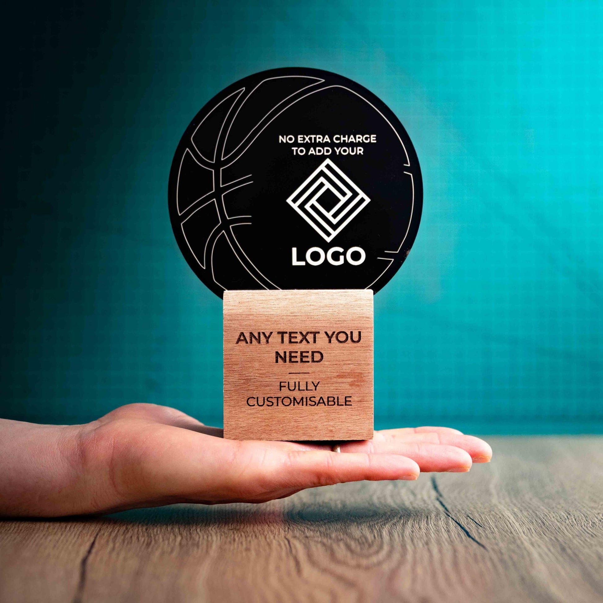 A medium Basketball trophy with custom text and logos, on an eco-friendly wooden base, with a black Perspex Basketball mounted on top, featuring fully customisable areas for text and logos, being held to show a size perspective.