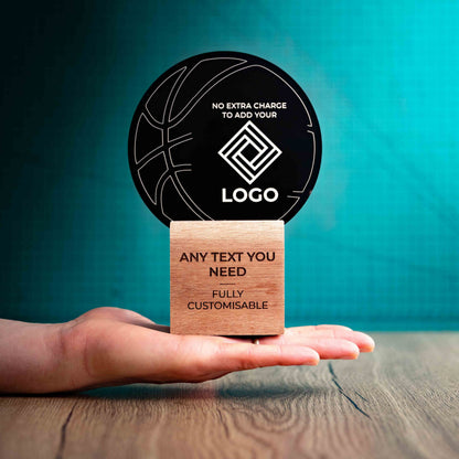 A medium Basketball trophy with custom text and logos, on an eco-friendly wooden base, with a black Perspex Basketball mounted on top, featuring fully customisable areas for text and logos, being held to show a size perspective.