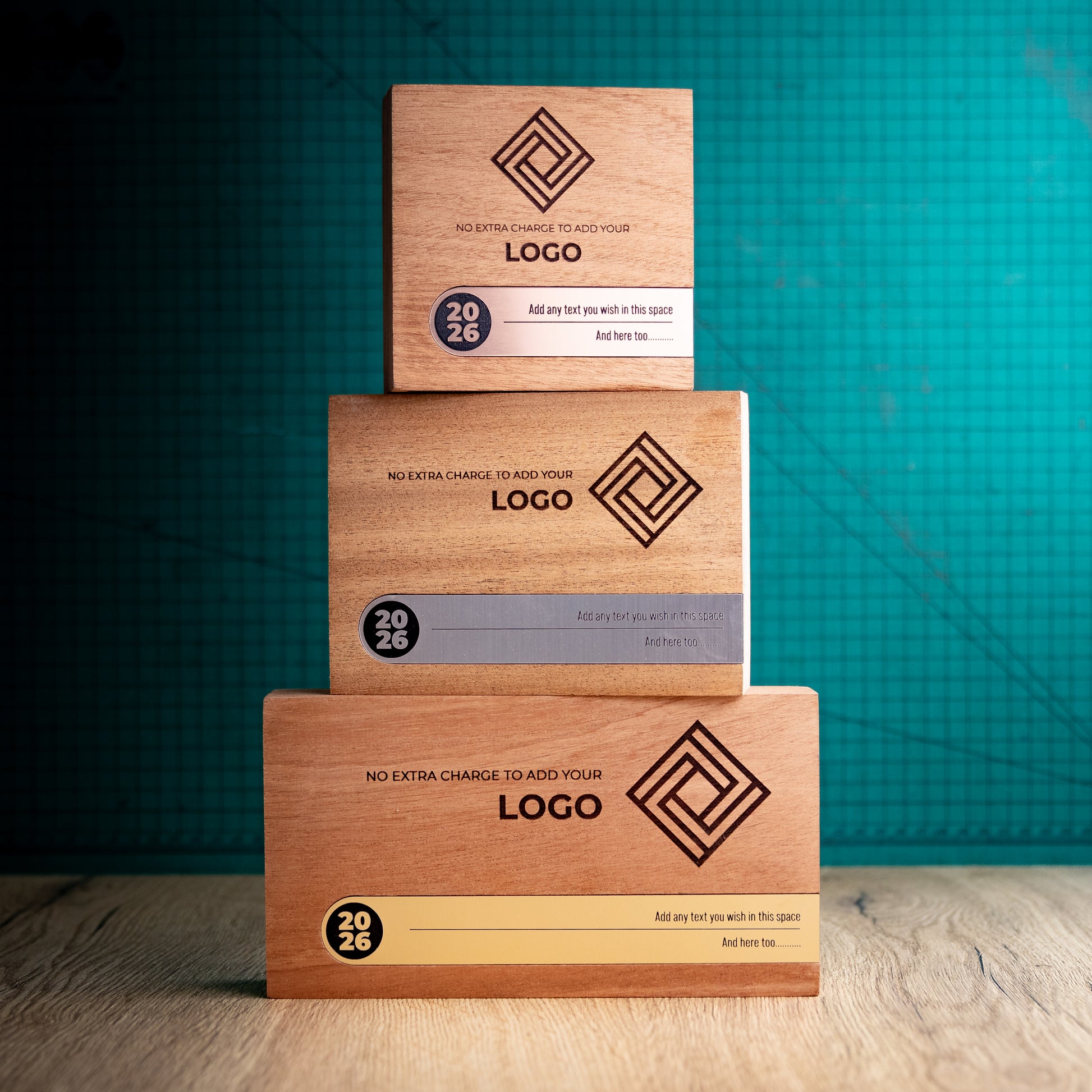 Three Bezel wooden trophies stacked by size, with a small bronze, medium silver and large gold design, each featuring an engraved logo and metallic personalisation inlay set into the front.