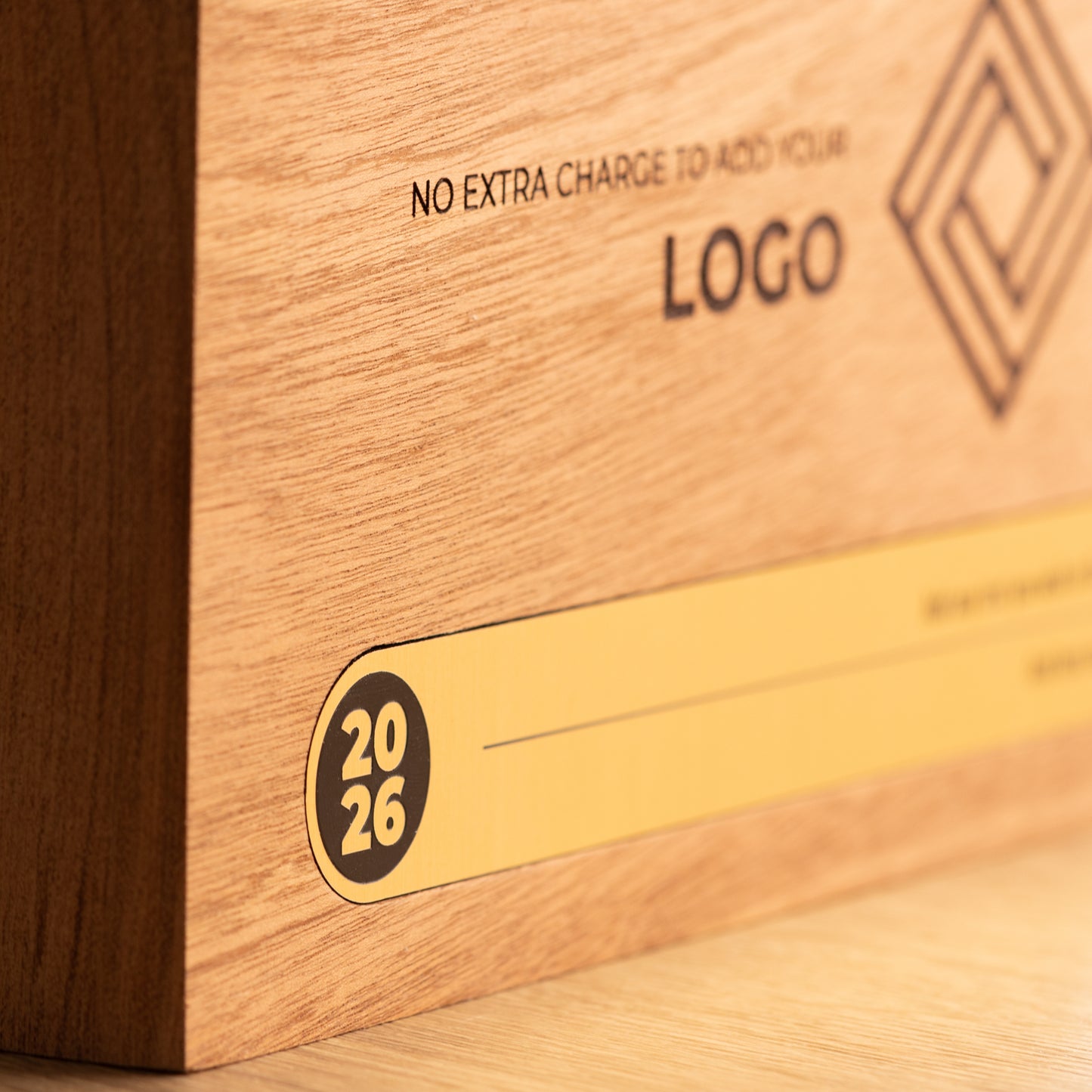 Shallow-focus close-up of the gold Bezel trophy inlay, focusing on the circular 2026 detail at the left while the engraved logo and personalisation area recede into the background.
