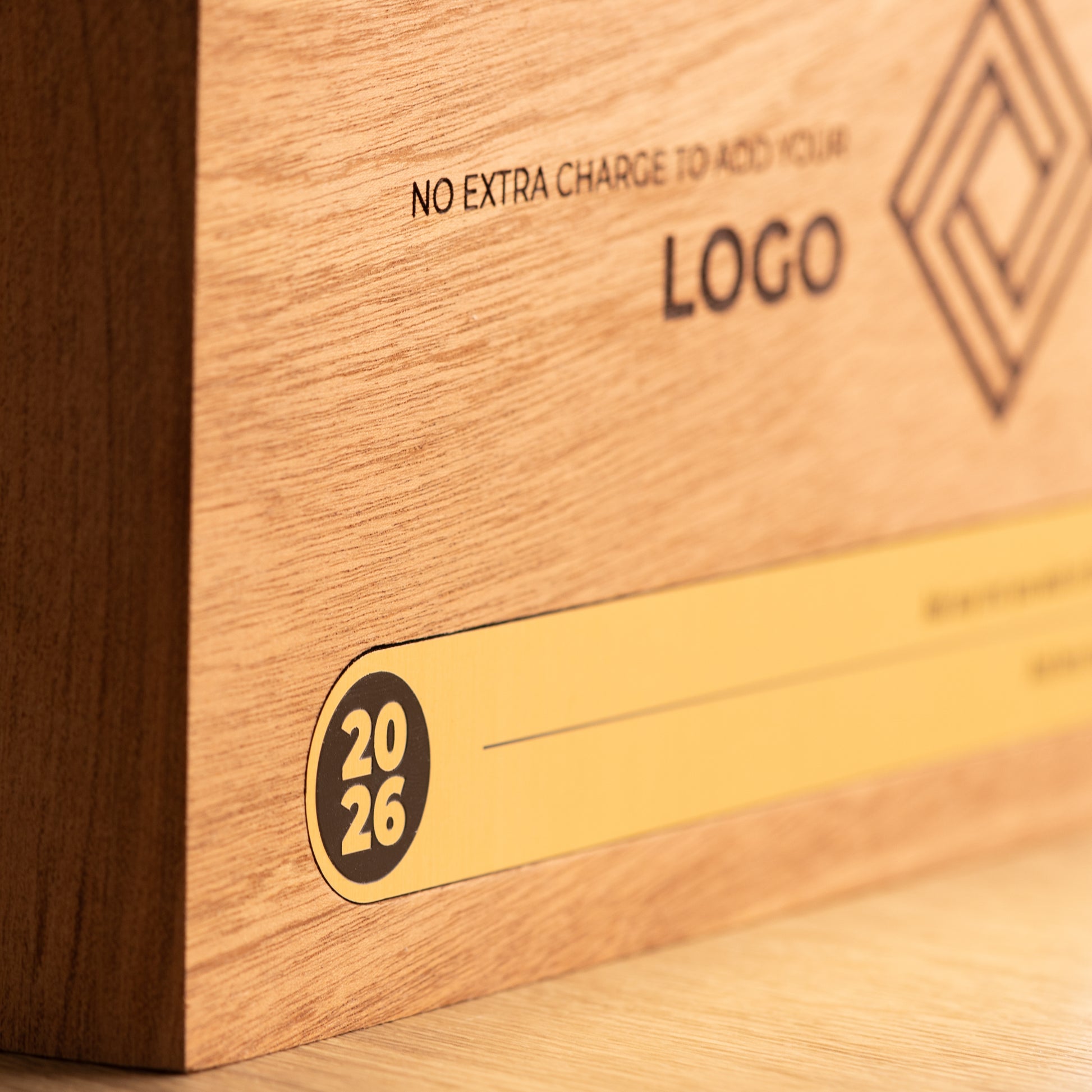 Shallow-focus close-up of the gold Bezel trophy inlay, focusing on the circular 2026 detail at the left while the engraved logo and personalisation area recede into the background.