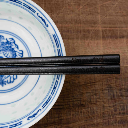 A pair of Japanese-style Chopsticks, colour black wood. The chopsticks are laser engraved and personalised with either a name or a phrase in English and are translated into either Chinese or Japanese.