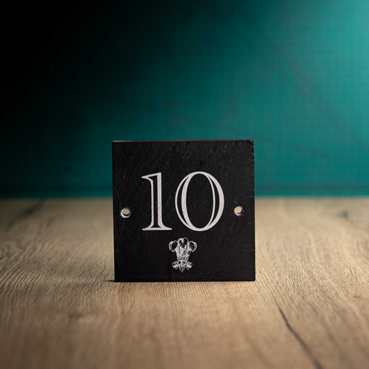 A laser-engraved square slate house sign on a wooden surface and teal background. Square 4.5" x 4.5"
