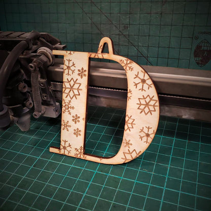 A wooden Christmas tree decoration laser cut into the shape of the letter "D" and engraved with snowflakes