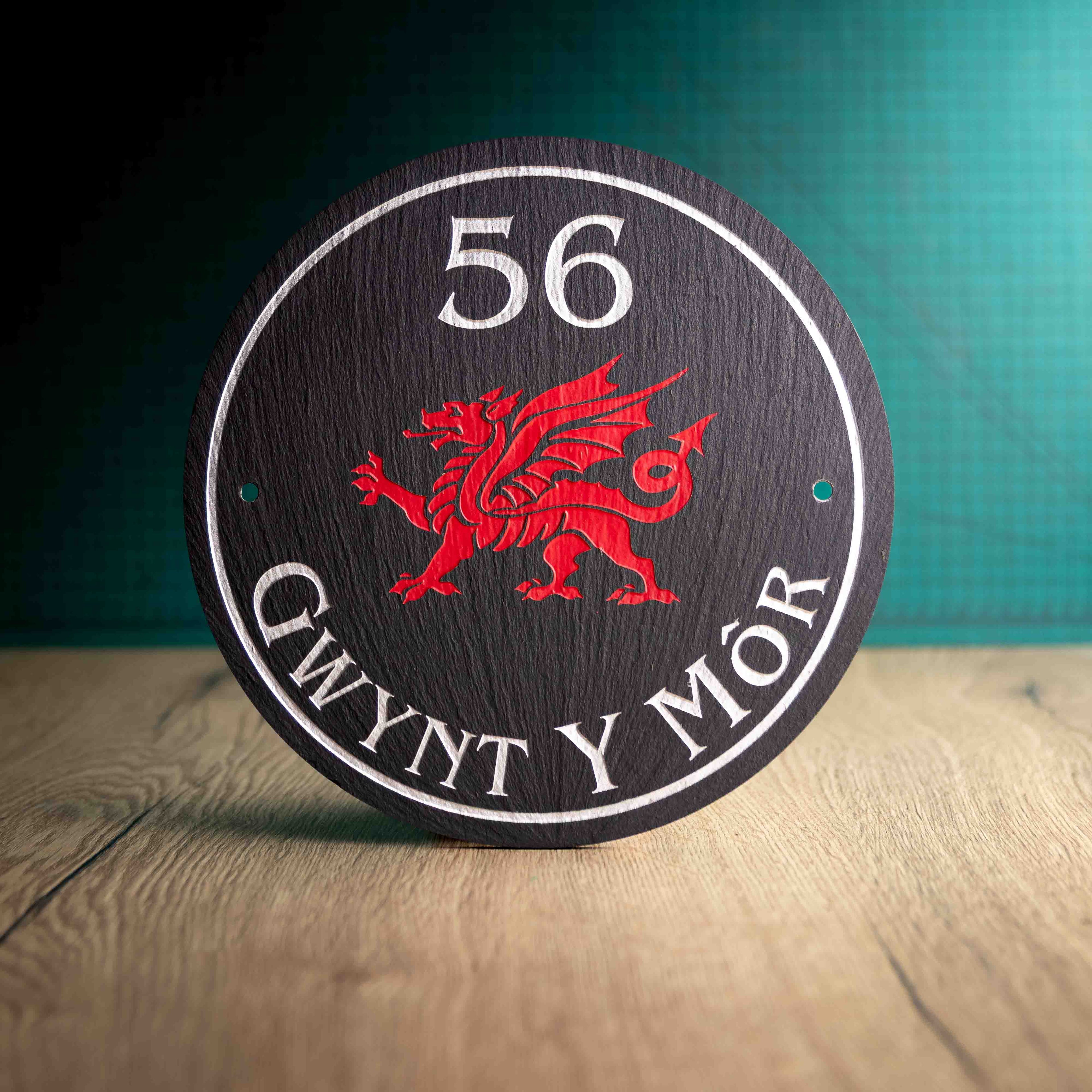 A circular Welsh Slate House Plaque with a colour filled house number, Welsh dragon and a border