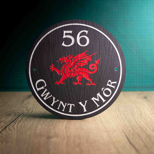 A circular Welsh Slate House Plaque with a colour filled house number, Welsh dragon and a border