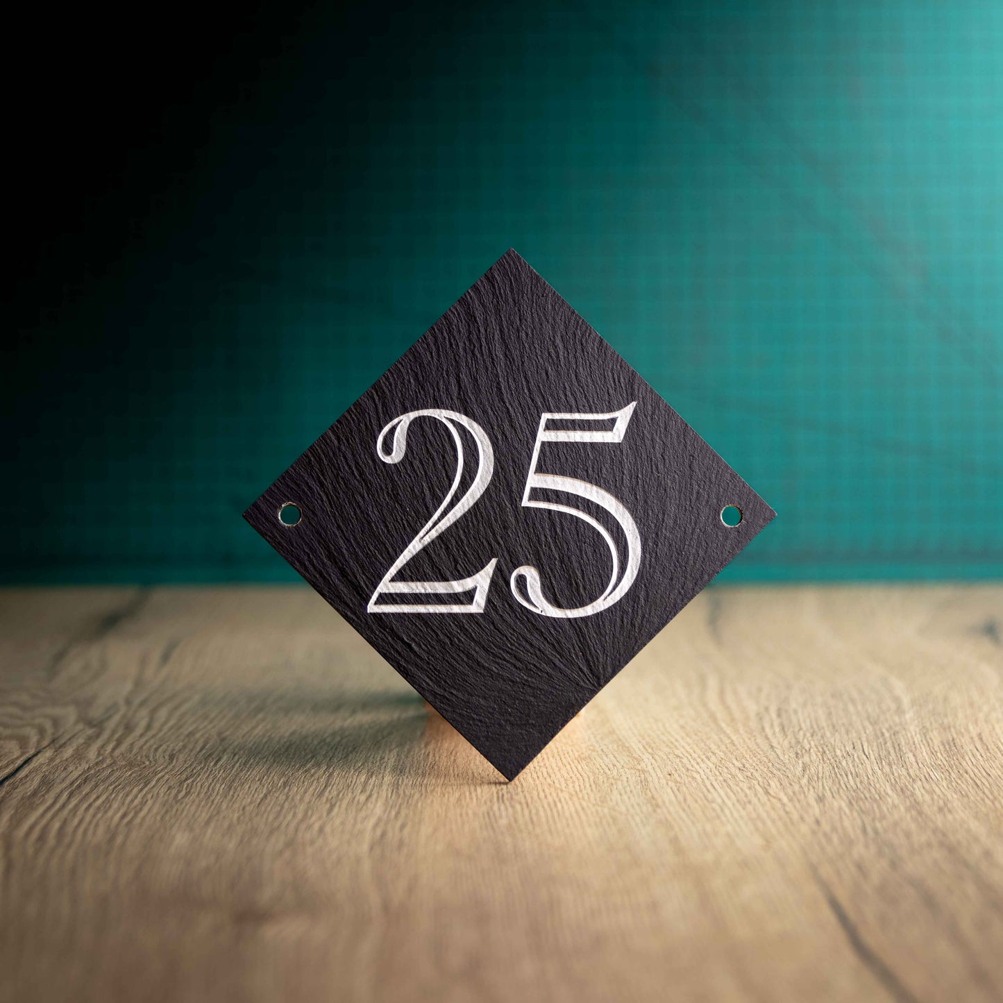 A colour-filled diamond slate house sign on a wooden surface and teal background. Diamond 4.5" x 4.5"