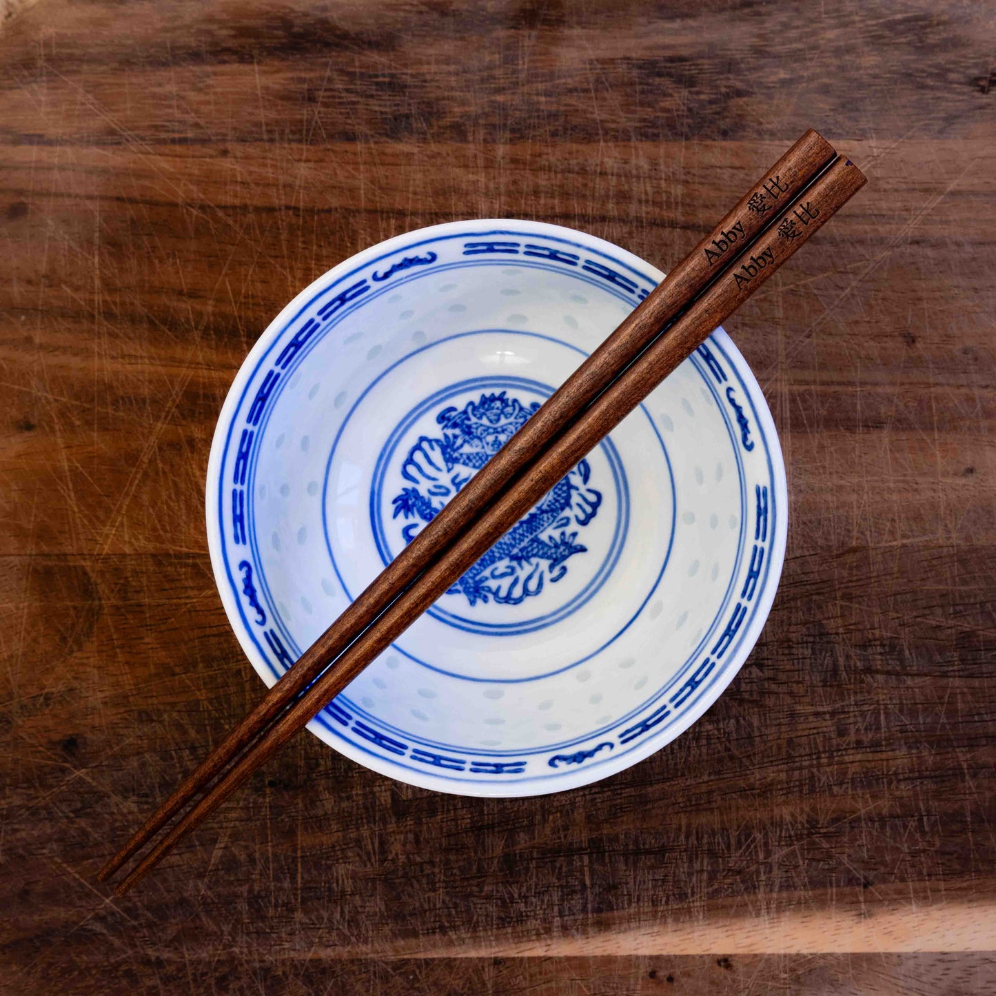 A pair of Japanese-style Chopsticks, colour dark wood. The chopsticks are laser engraved and personalised with either a name or a phrase in English and are translated into either Chinese or Japanese.
