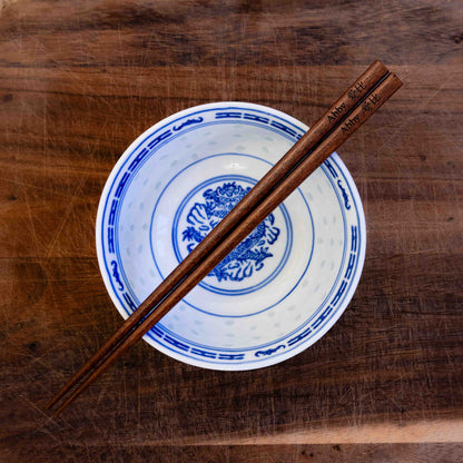 A pair of Japanese-style Chopsticks, colour dark wood. The chopsticks are laser engraved and personalised with either a name or a phrase in English and are translated into either Chinese or Japanese.