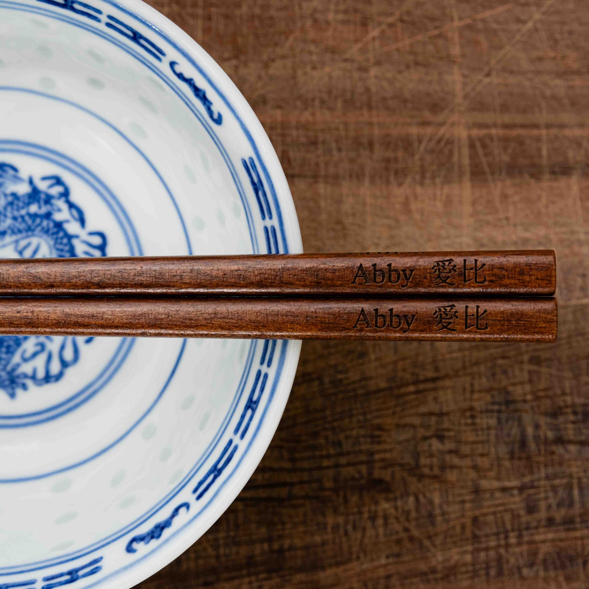A pair of Japanese-style Chopsticks, colour dark wood. The chopsticks are laser engraved and personalised with either a name or a phrase in English and are translated into either Chinese or Japanese.