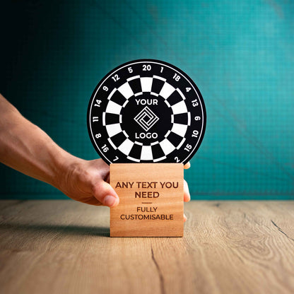 A hand holding a large darts trophy with custom text and logos, on an eco-friendly wooden base, with a black Perspex dart board mounted on top, featuring fully customisable areas for text and logos.