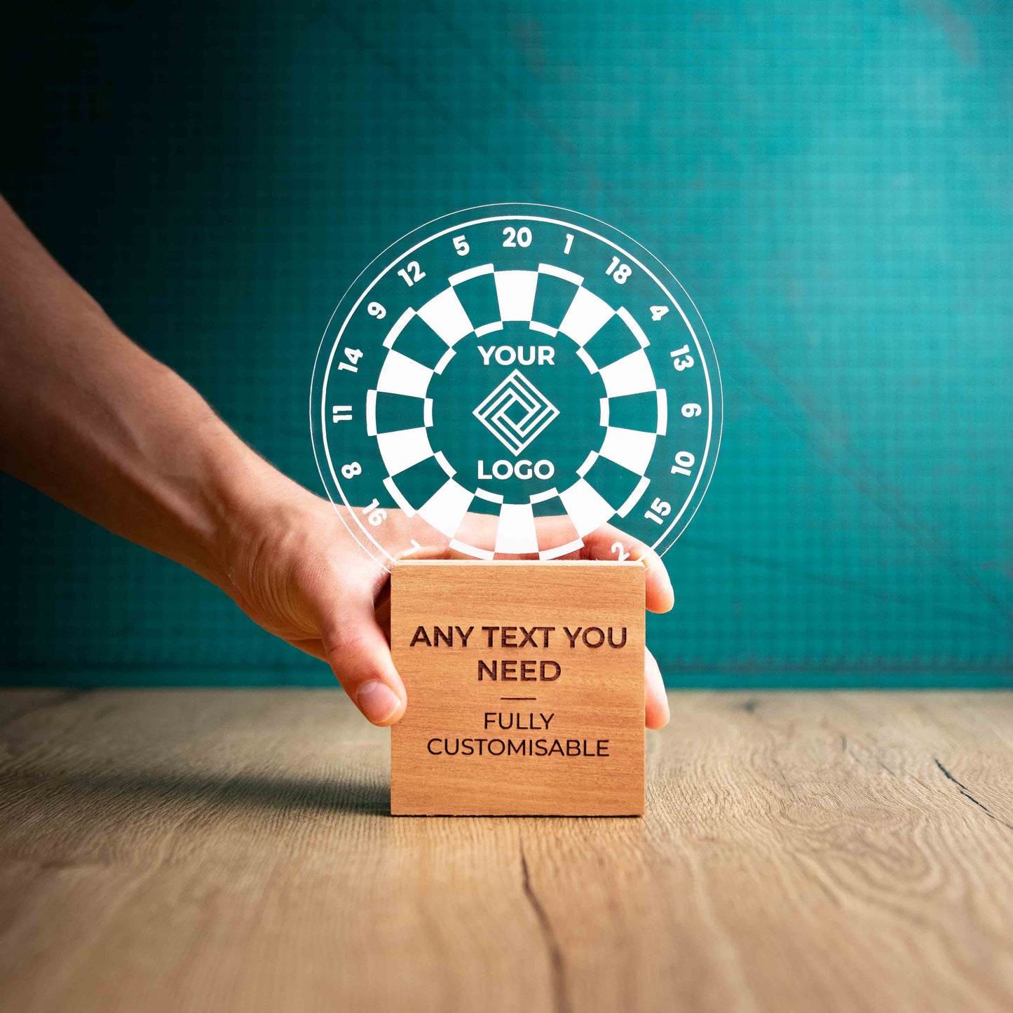 A hand holding a large darts trophy with custom text and logos, on an eco-friendly wooden base, with a clear Perspex dart board mounted on top, featuring fully customisable areas for text and logos.